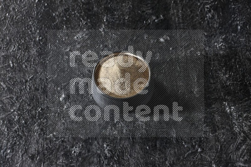 Black pottery bowl full of white pepper powder on textured black flooring