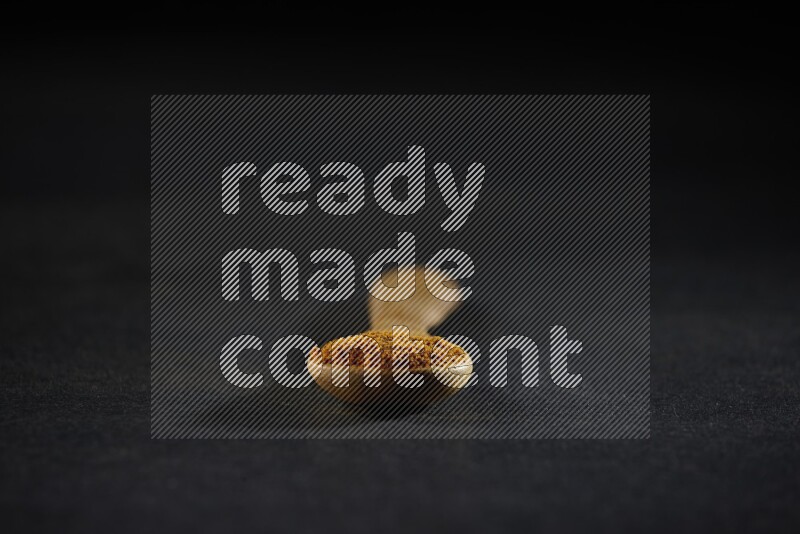 A wooden spoon full of turmeric powder on black flooring