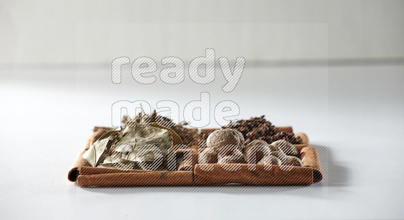 4 squares of cinnamon sticks full of bay laurel leaves, dried basil, cloves and nutmegs on white flooring