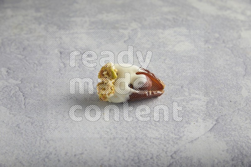 Hazulnut stuffed date covered with white chocolate and crushed peanuts & pistachios on light grey background