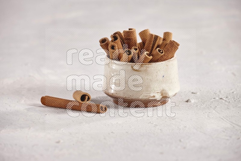 Cinnamon sticks in a beige bowl and more sticks beside it on white background