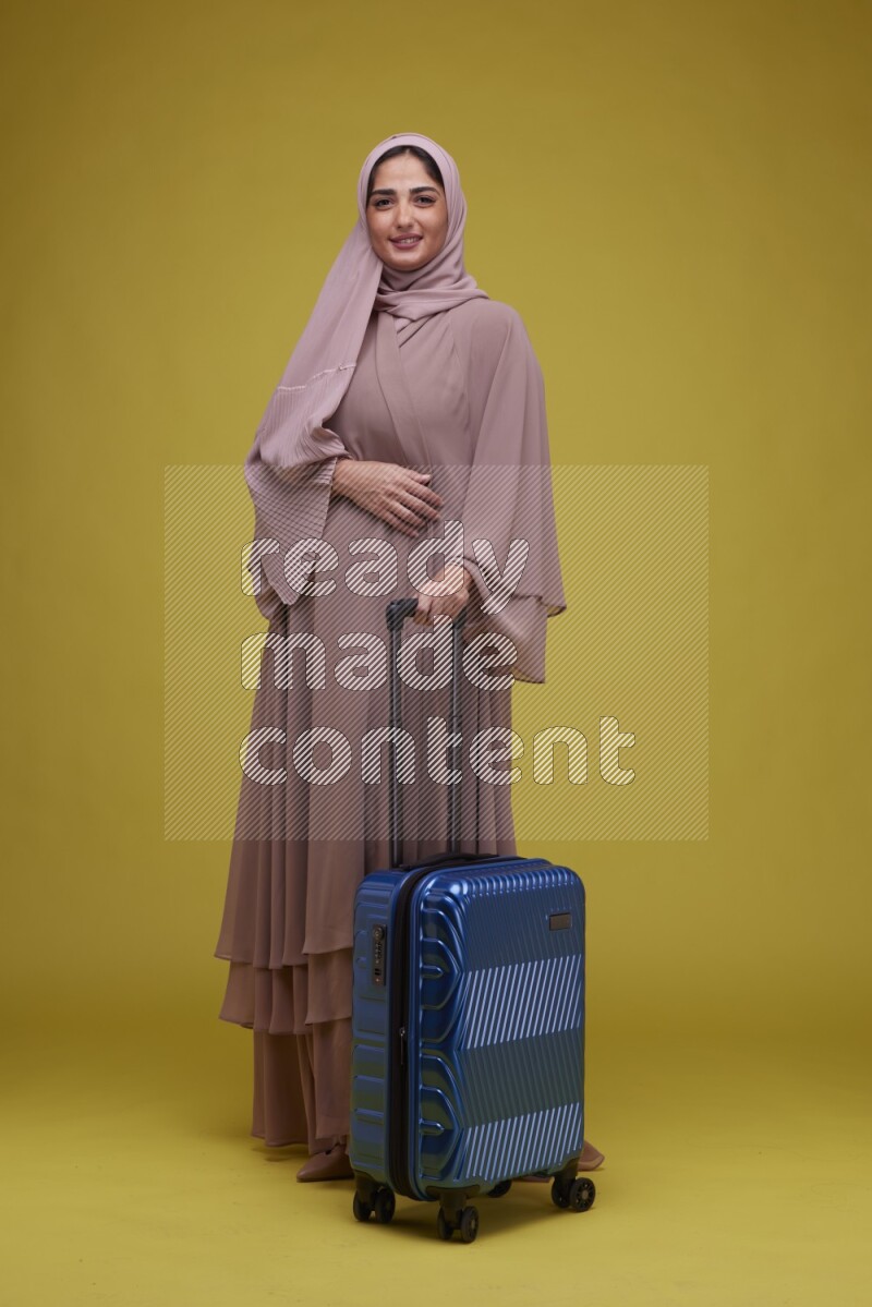 A woman With suit Case on a Yellow Background wearing Brown Abaya with Hijab