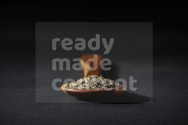 A wooden ladle full of cumin seeds on black flooring