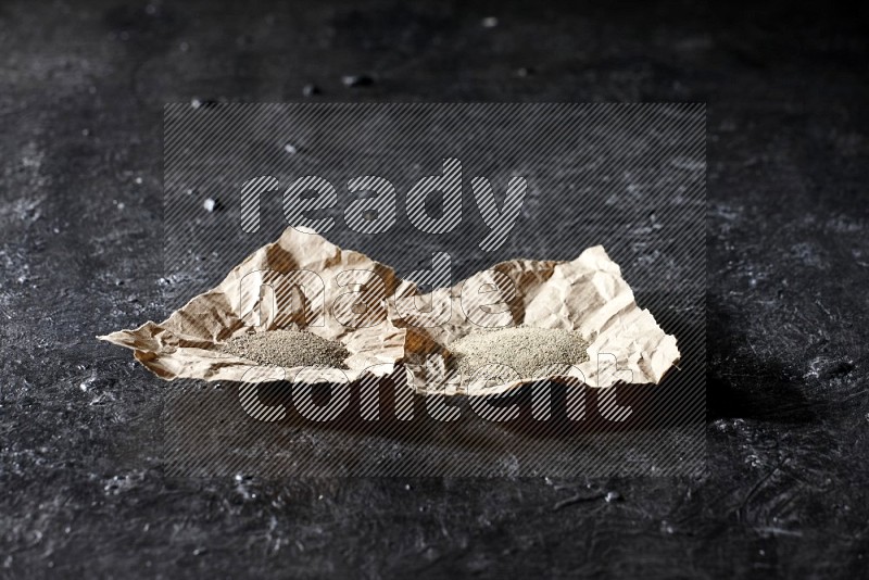 2 Crumpled pieces of paper full of black and white pepper powder on a textured black flooring