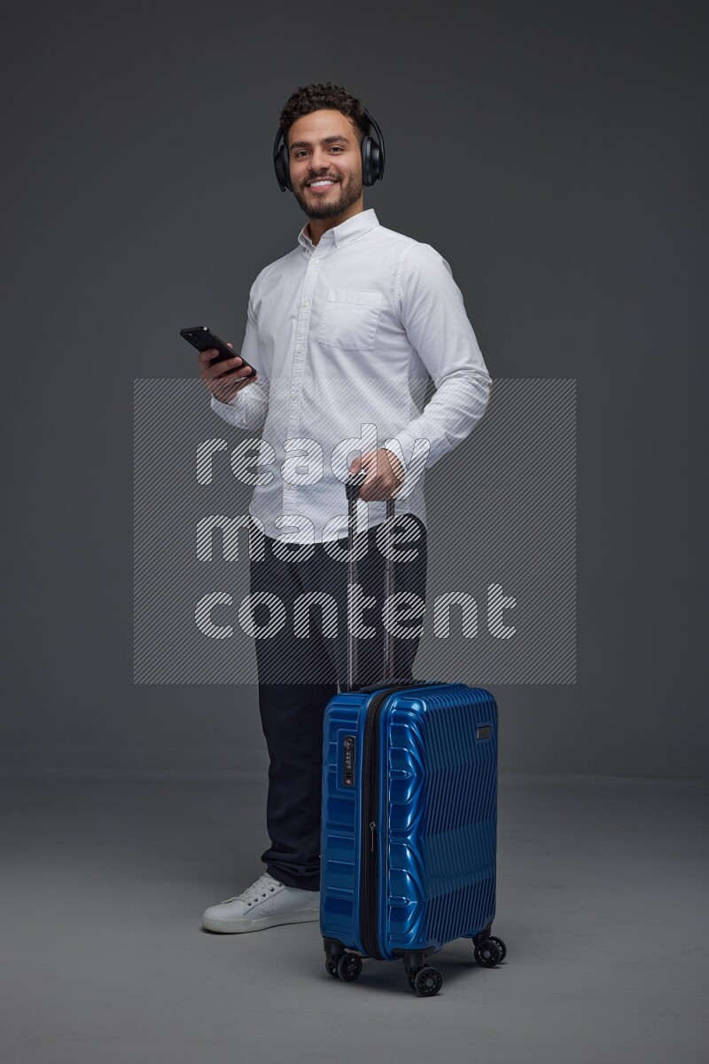 A man wearing smart casual and headphone holding luggage eye level on a gray background