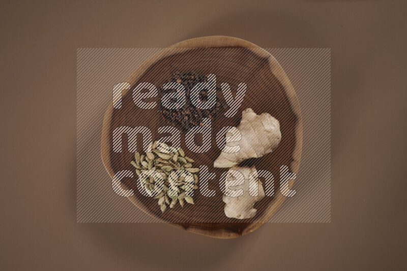 An assorted whole spices on a flat wooden tray including fresh and dried ginger, cinnamon sticks, cardamom, turmeric fingers, cloves, star anise on beige background