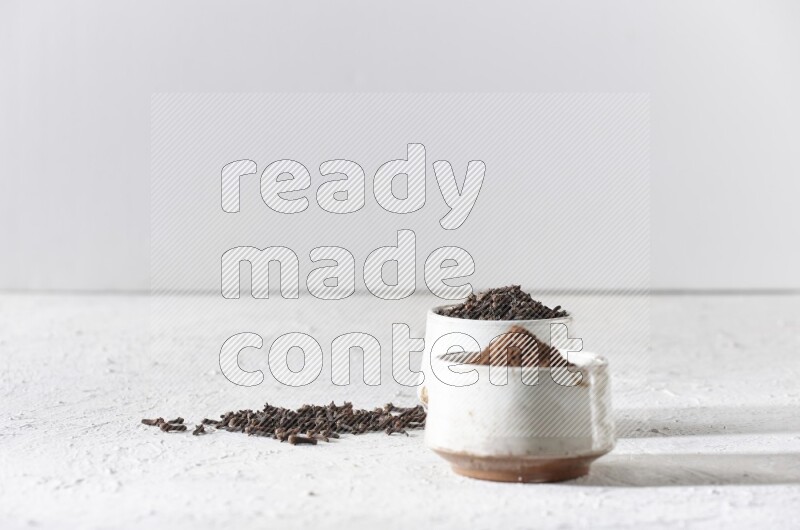 2 Beige ceramic bowls, one full of cloves and the other full of powder on textured white flooring