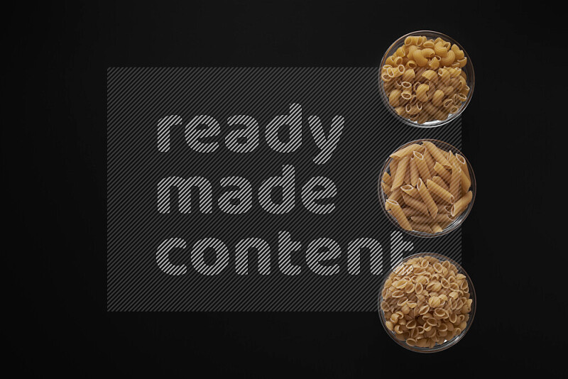 Different pasta types in 3 glass bowls on black background