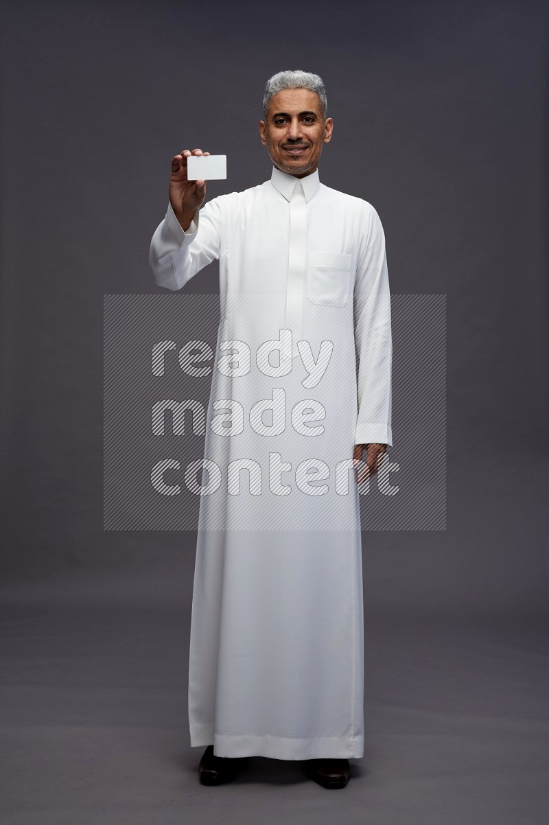 Saudi man wearing thob standing holding ATM card on gray background