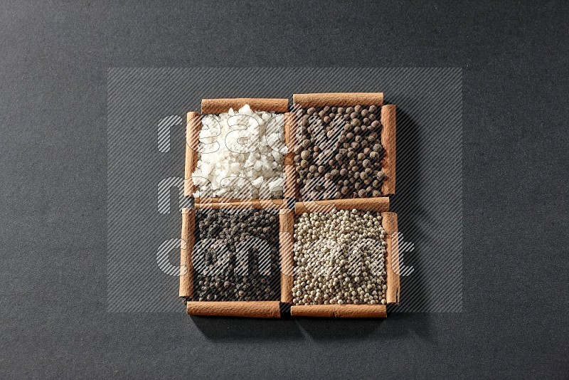 4 squares of cinnamon sticks full of black pepper, white pepper, allspice and white salt on black flooring