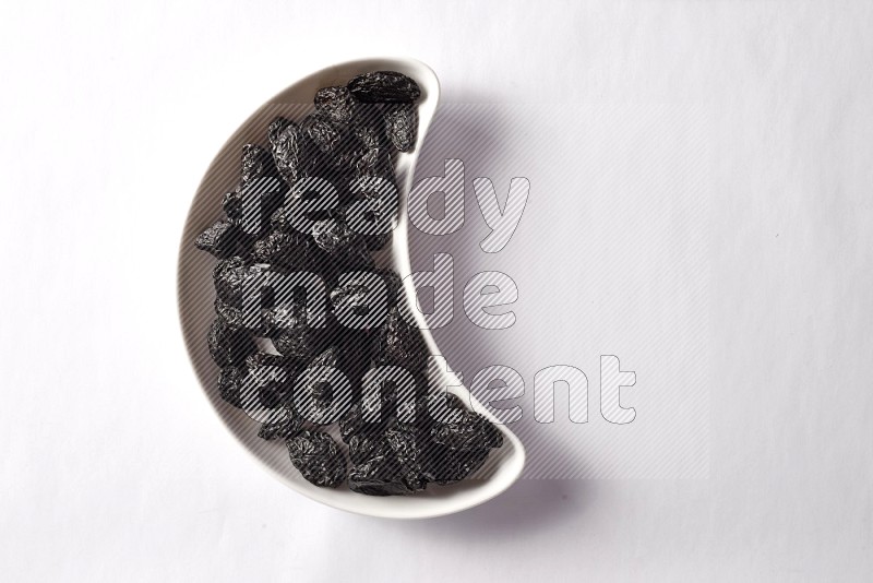Dried plums in a crescent pottery plate on white background
