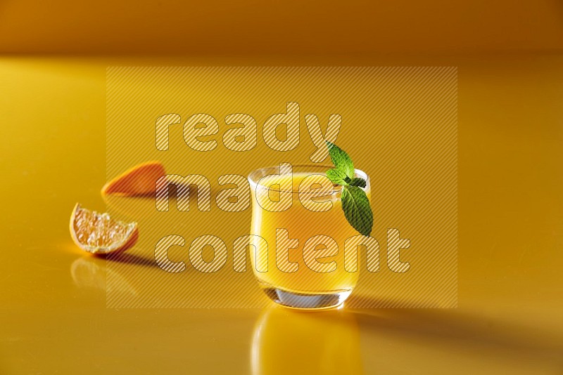 glass of orange juice with  mint on yellow background