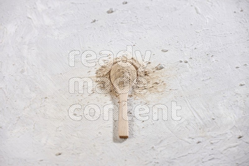 A wooden spoon full of garlic powder surrounded by the powder on a textured white flooring in different angles