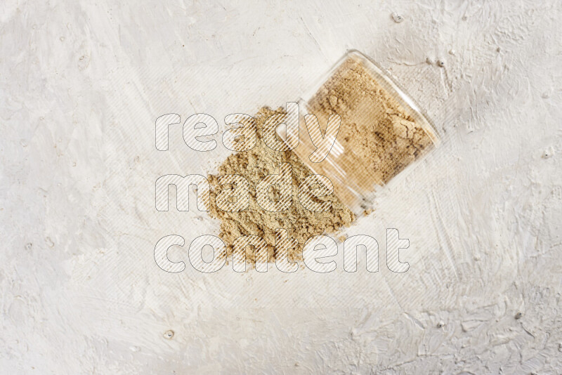 A glass jar full of ground ginger powder flipped with some spilling powder on white background