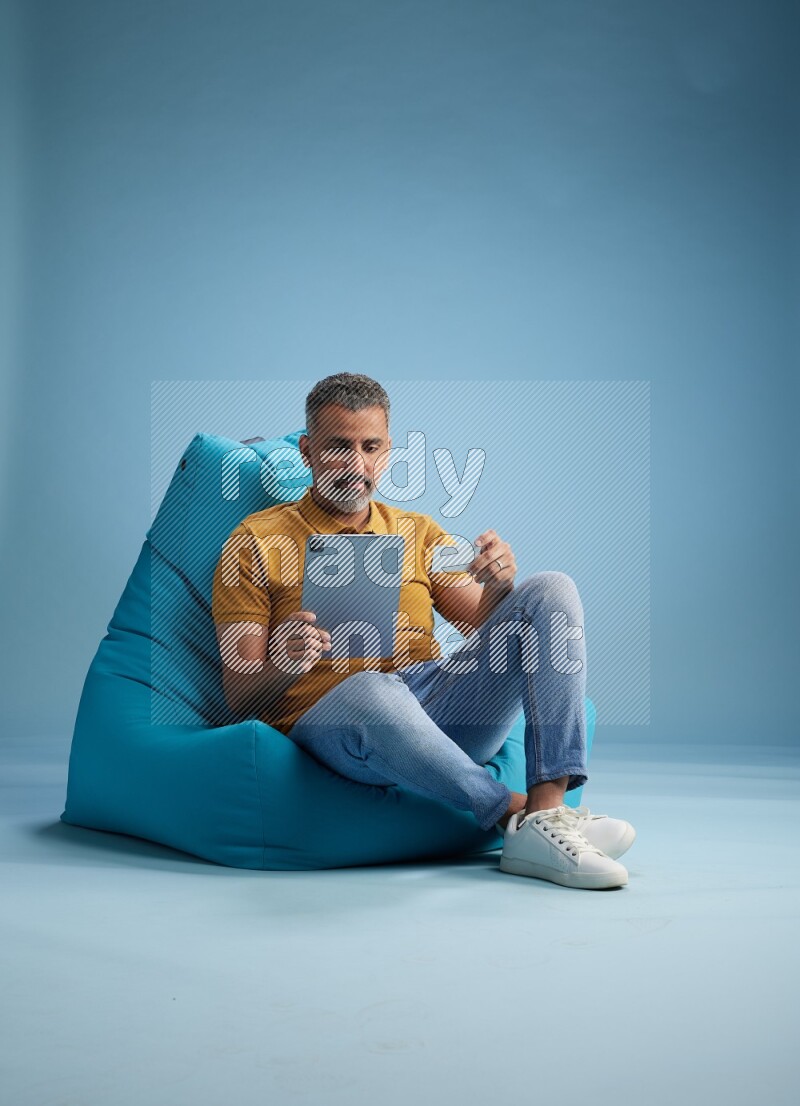 A man sitting on a blue beanbag and holding ATM card with tablet