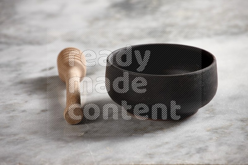 Black Pottery Bowl with wooden honey handle on the side with grey marble flooring, 15 degree angle