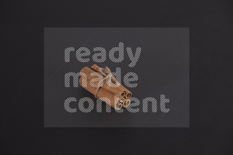 4 Cinnamon sticks stacked and bounded on black flooring