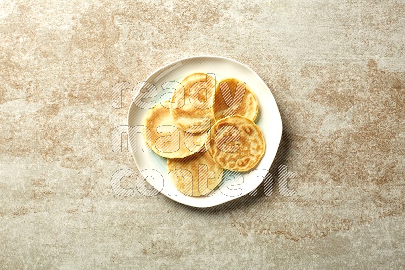 Five stacked plain mini pancakes in a bicolor plate on beige background