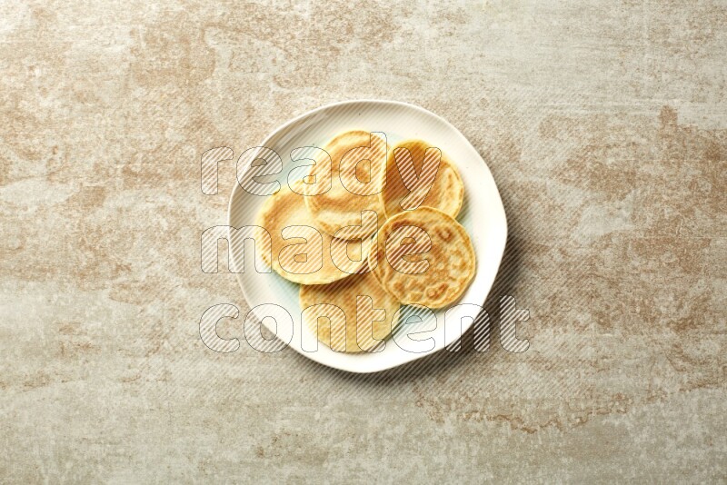 Five stacked plain mini pancakes in a bicolor plate on beige background