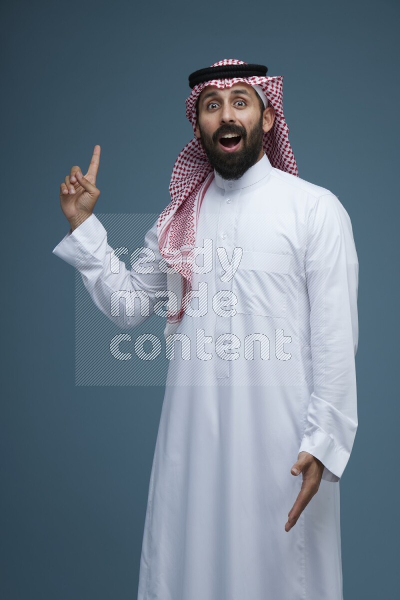 A man pointing in a blue background wearing Saudi Thob and Shomag