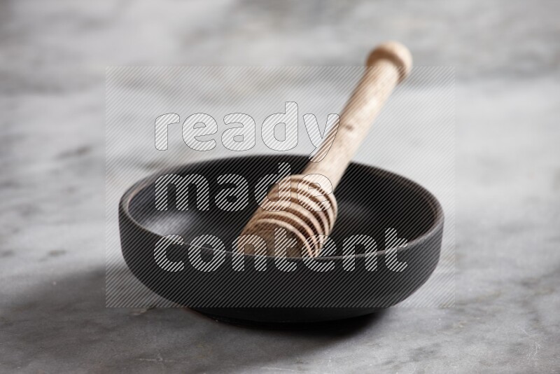 Black pottery bowl with wooden honey dipper in it on grey marble background