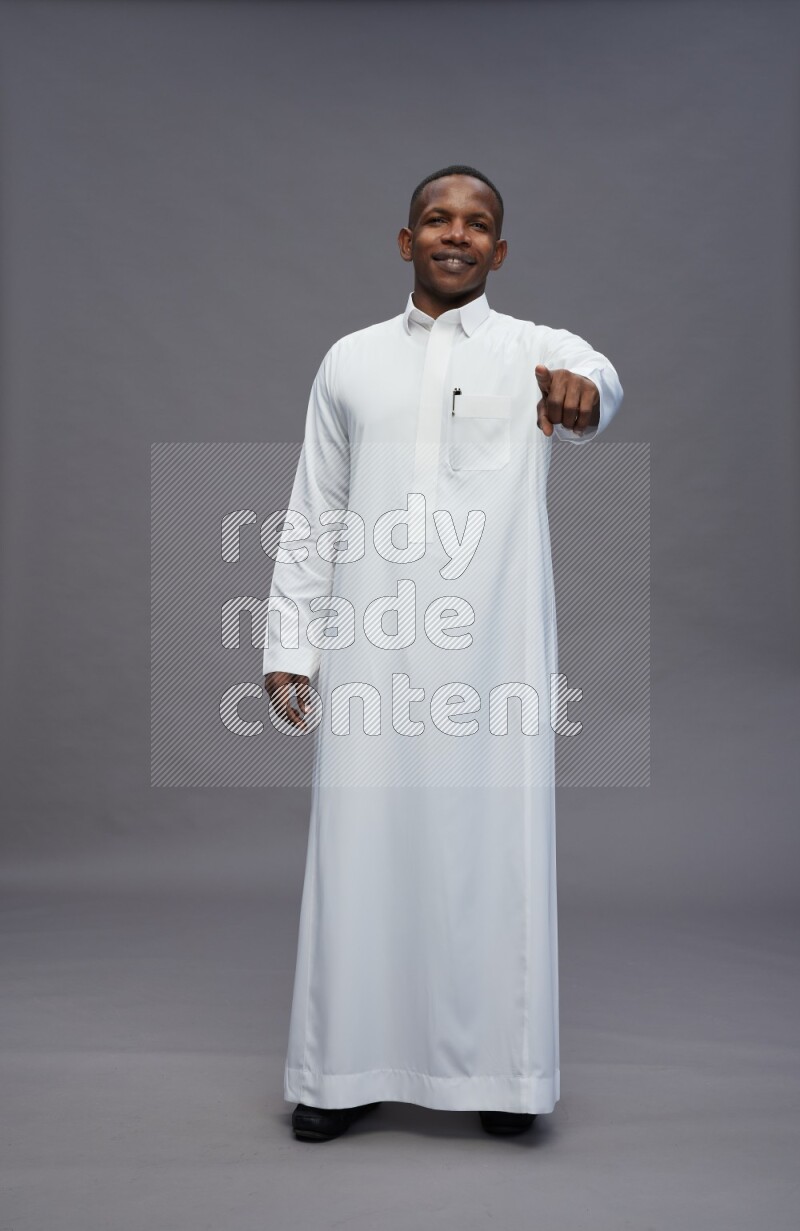 Saudi man wearing thob standing interacting with the camera on gray background