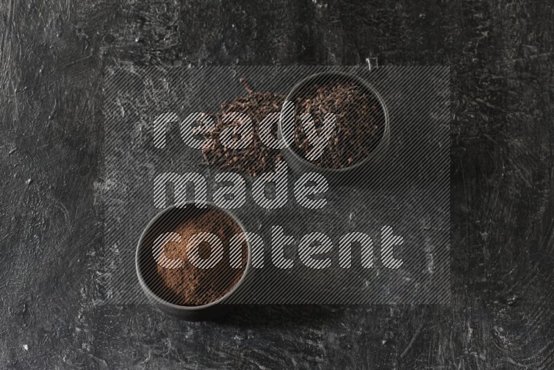 وعاءين من الفخار الأسود أحدهما ممتلئي بحبوب القرنفل والآخر ممتلئ ببودرة القرنفل على خلفية سوداء