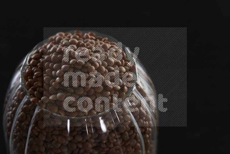 Brown lentils in a glass jar on black background