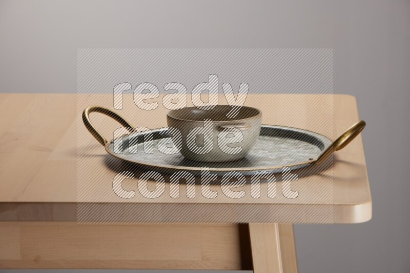 off white bowl placed on a rounded stainless steel tray with golden handels on the edge of wooden table