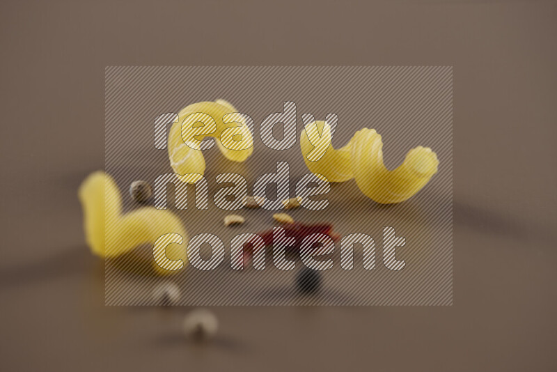 معكرونة مع مكونات متنوعة من الطماطم والثوم والبصل والفلفل الأحمر والفلفل الأسود والفلفل الأبيض وأوراق الغار وإكليل الجبل والهيل على خلفية بيج