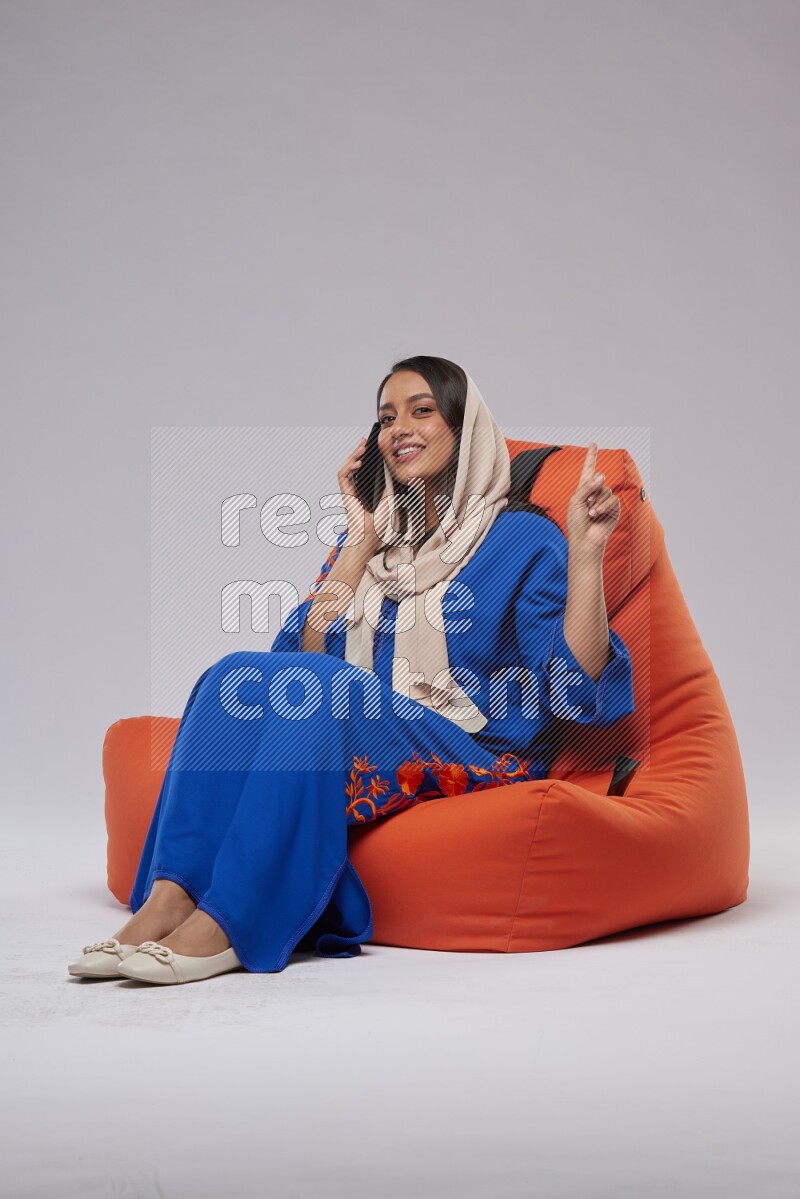 A Saudi woman wearing Jalabiya sitting on an orange beanbag and talking on the phone