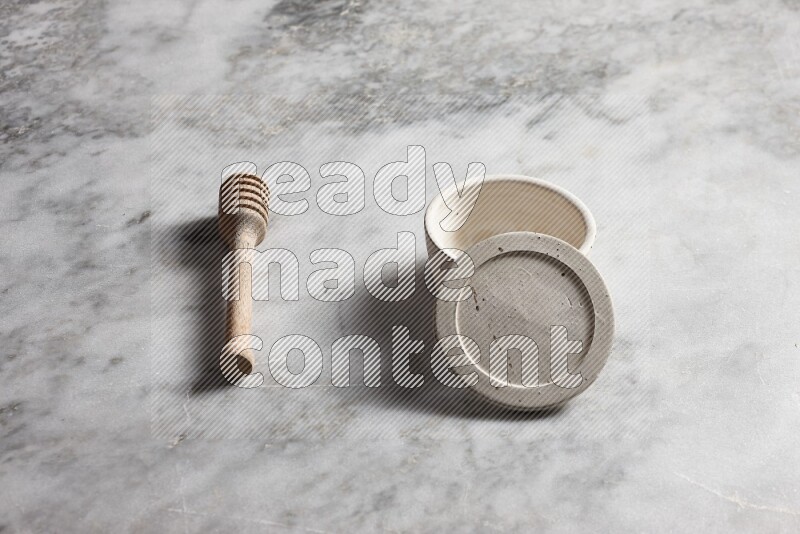 White pottery bowl with wooden honey dipper on the side on grey marble background