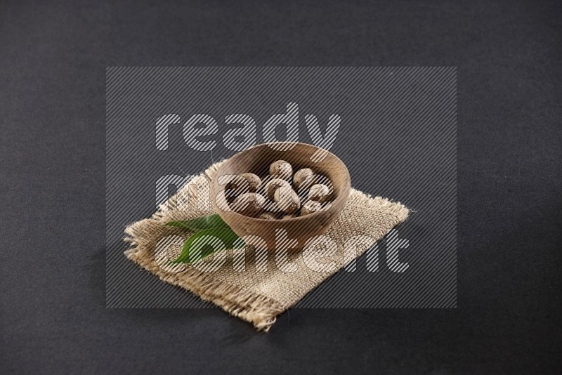 A wooden bowl full of nutmeg on burlap fabric on a black flooring in different angles