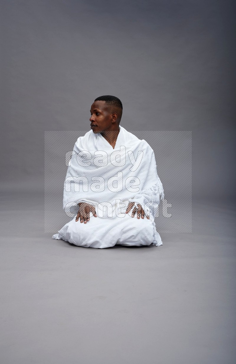A man wearing Ehram sitting on floor praying on gray background