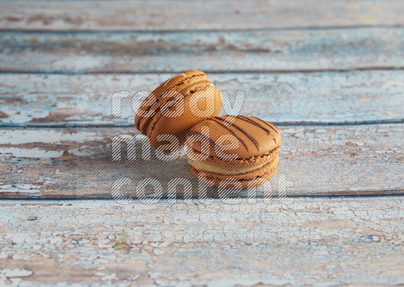 45º Shot of of two assorted Brown Irish Cream, and light brown Almond Cream macarons next to each other on light blue background