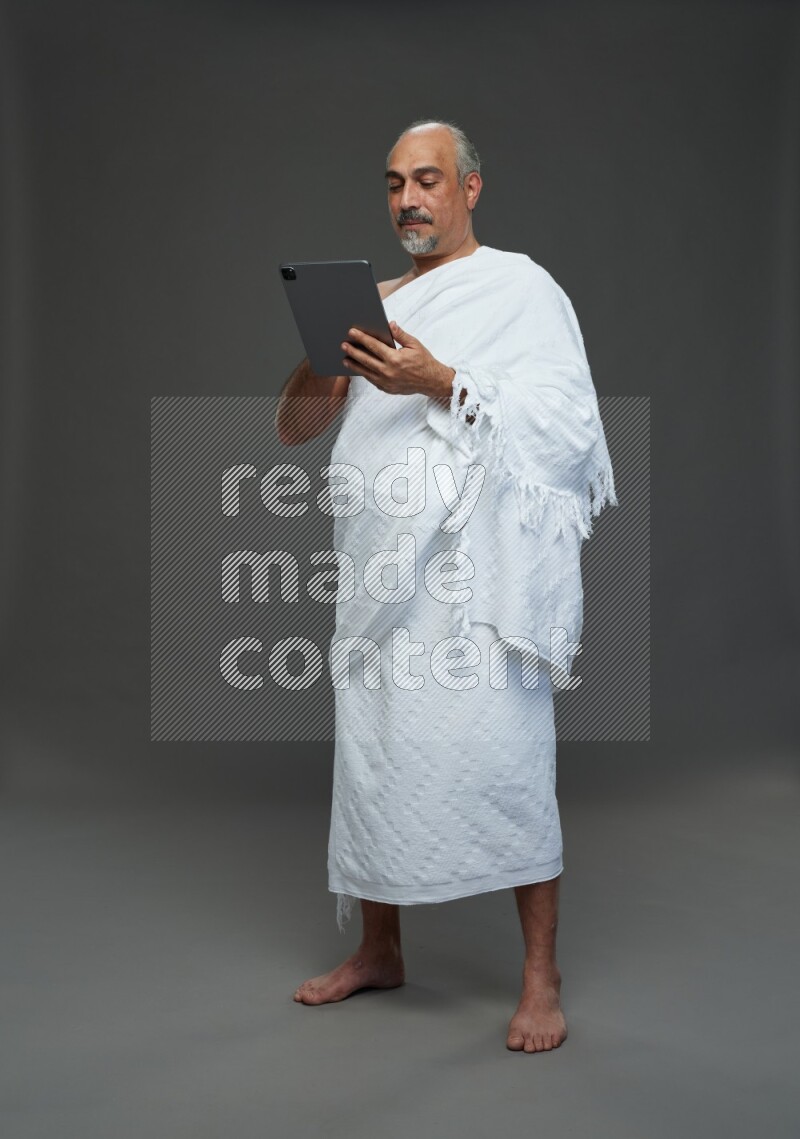 A man wearing Ehram Standing working on tablet on gray background