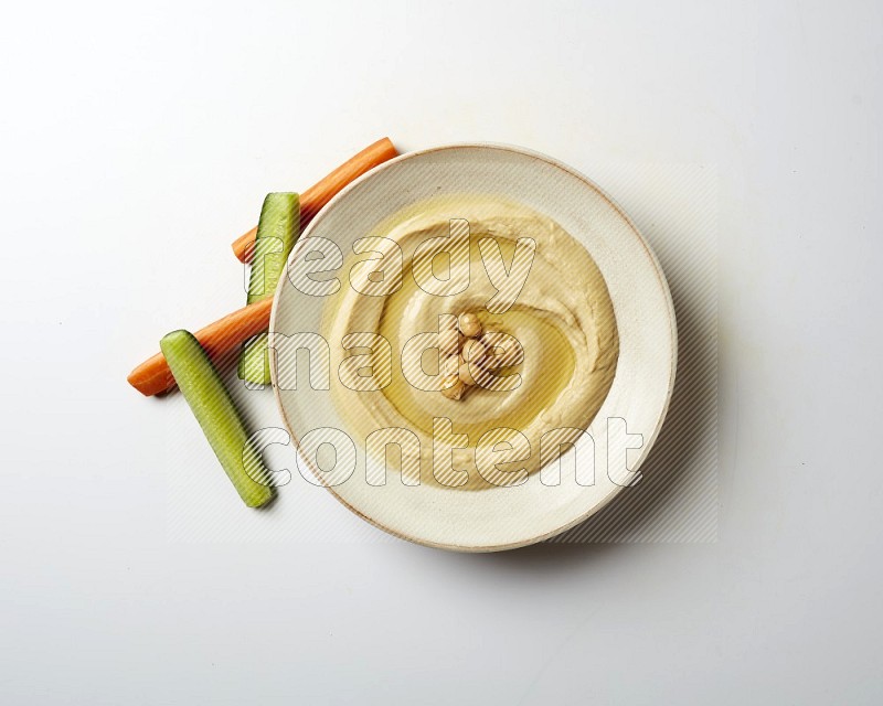 Hummus in a pottry plate garnished with roasted chickpeas on a white background