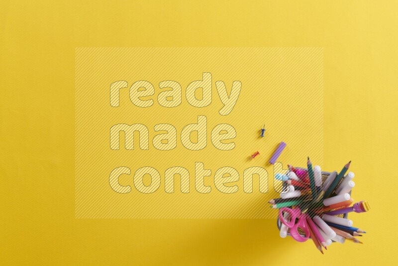 Pens, pencils and school supplies in a metal pen holder on yellow background