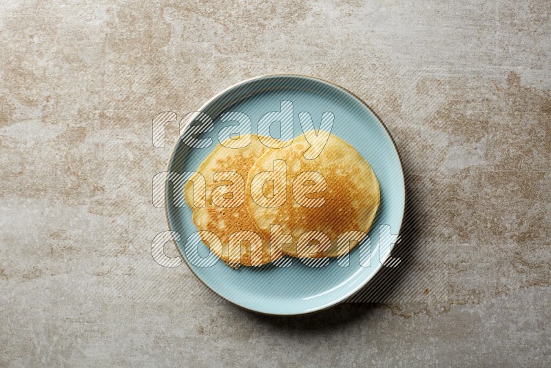Two stacked plain pancakes in a blue plate on beige background