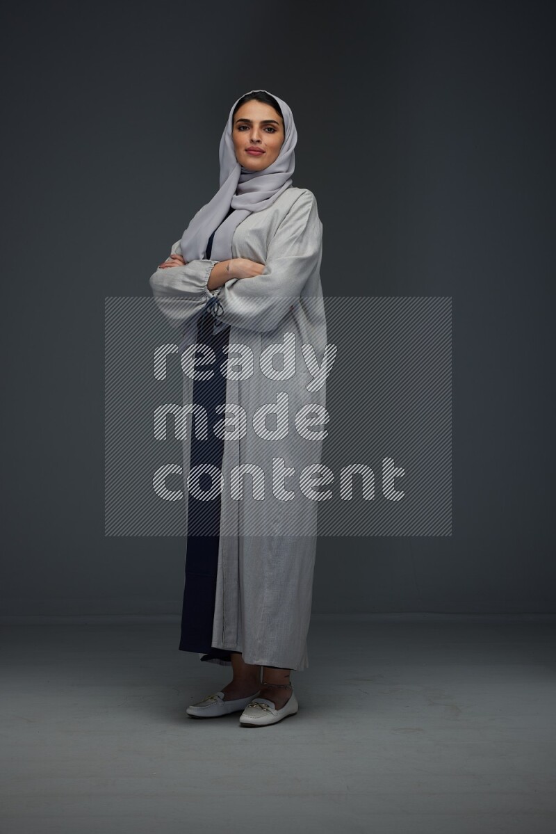 A Saudi woman wearing a light gray Abaya and head scarf standing and making multi poses eye level on a grey background