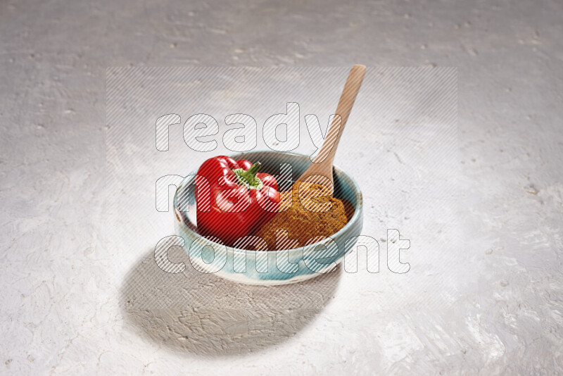 A colored pottery plate full of ground paprika powder and red bell pepper on white background