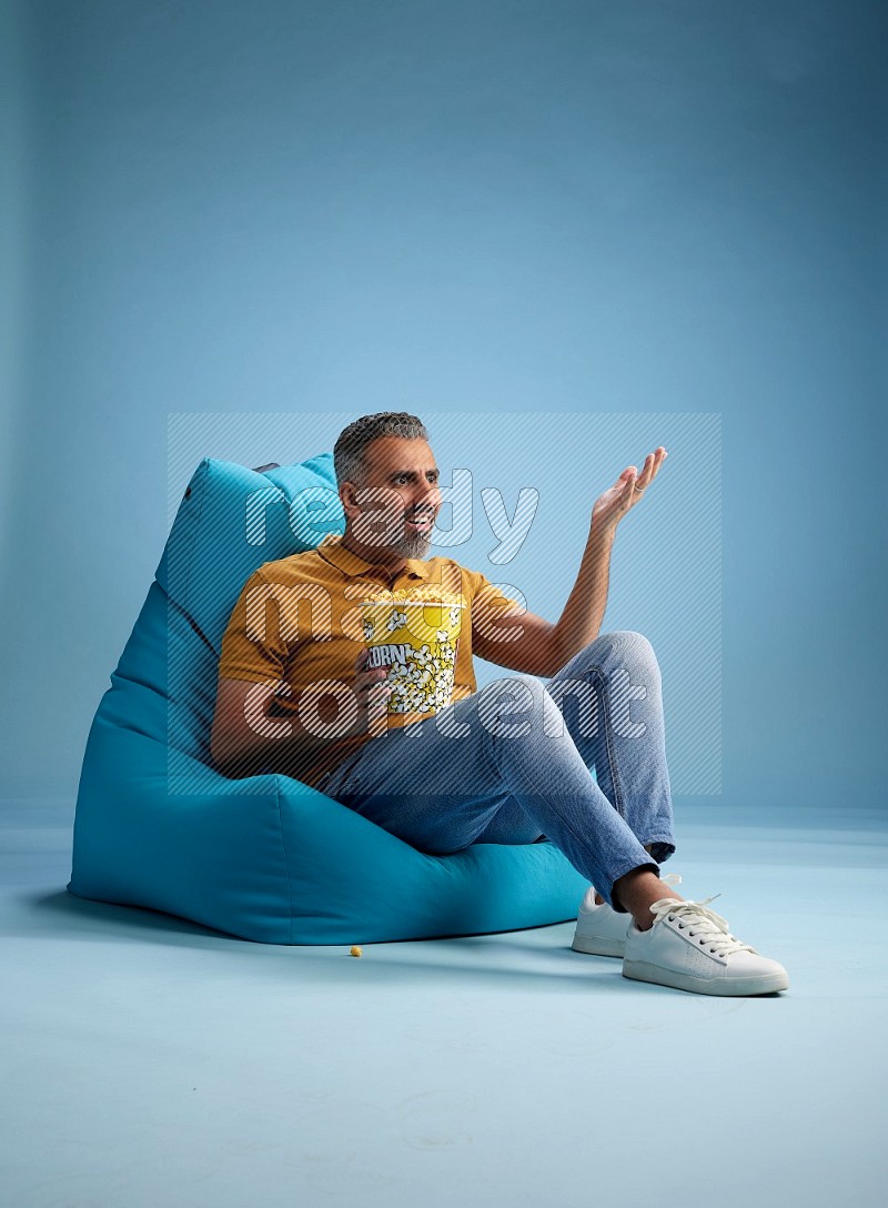 A man sitting on a blue beanbag and eating popcorn