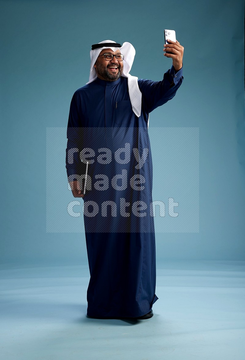Saudi Man with shimag Standing taking selfie on blue background