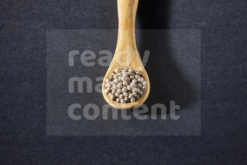 A wooden spoon full of white pepper beads on black flooring