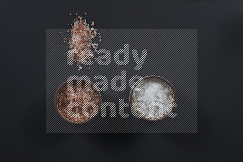 2 وعاء فخاري احدهمها ممتلئ بملح الهيمالايا والأخر بالملح الأبيض على خلفية سوداء