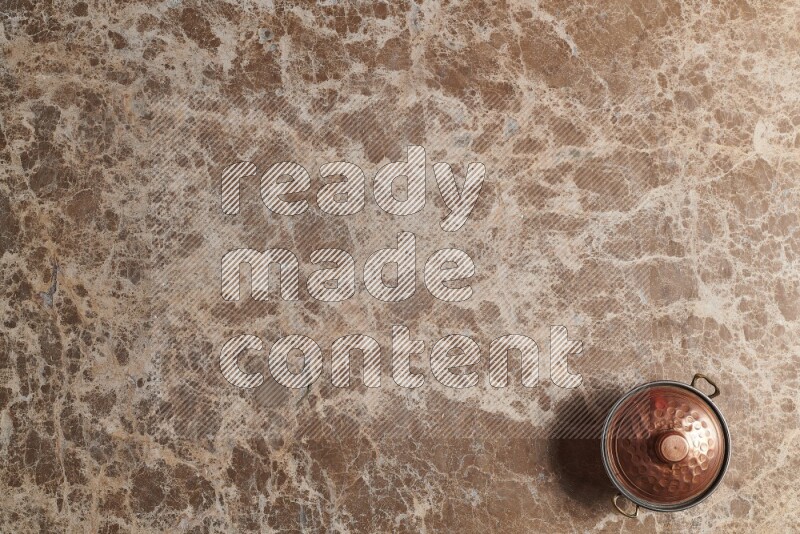 A small copper pot on beige marble background