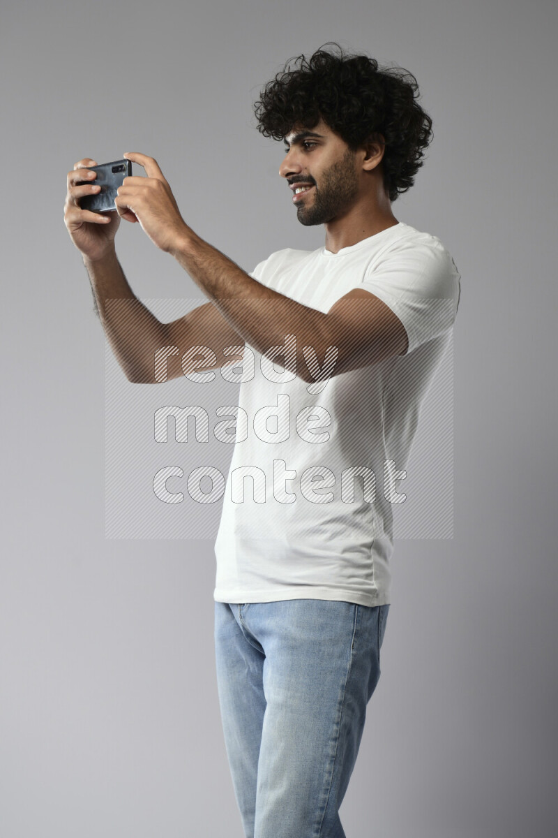 A man wearing casual standing and shooting with his phone on white background