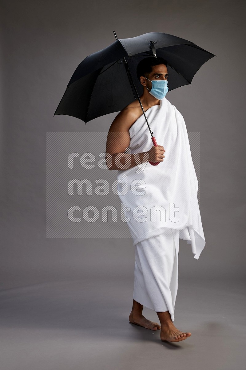 A man wearing Ehram and mask Standing holding umbrella on gray background on gray background