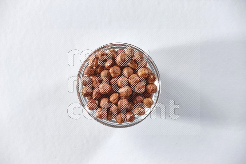 A glass bowl full of peeled hazelnuts on a white background in different angles