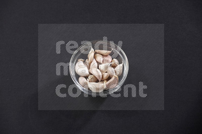 A glass bowl full of garlic cloves on a black flooring